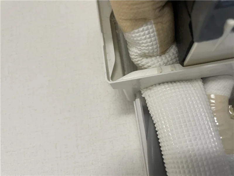 エアコンの室内機の下の枠に押されて、つぶれているドレンホース