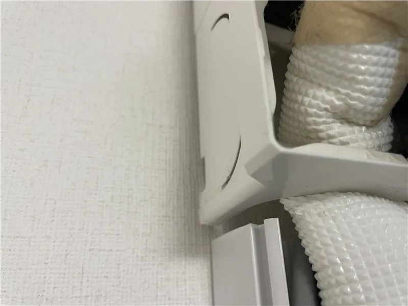 エアコンの室内機の下の枠の角に、ドレンホースが押されているところ